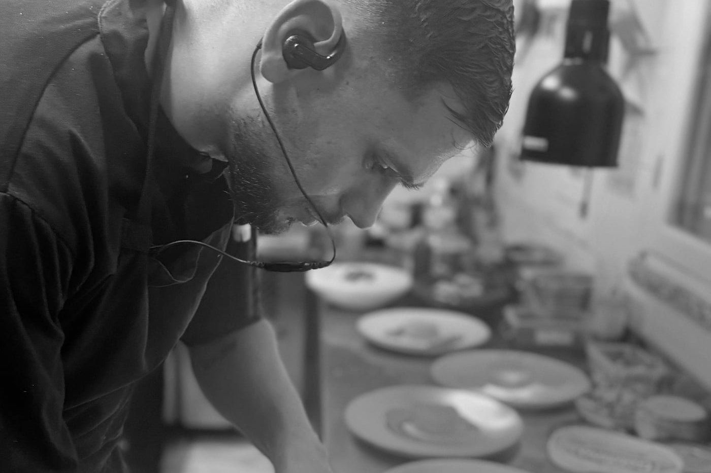 Le chef penché sur le plan de travail de sa cuisine, assiettes alignées devant lui