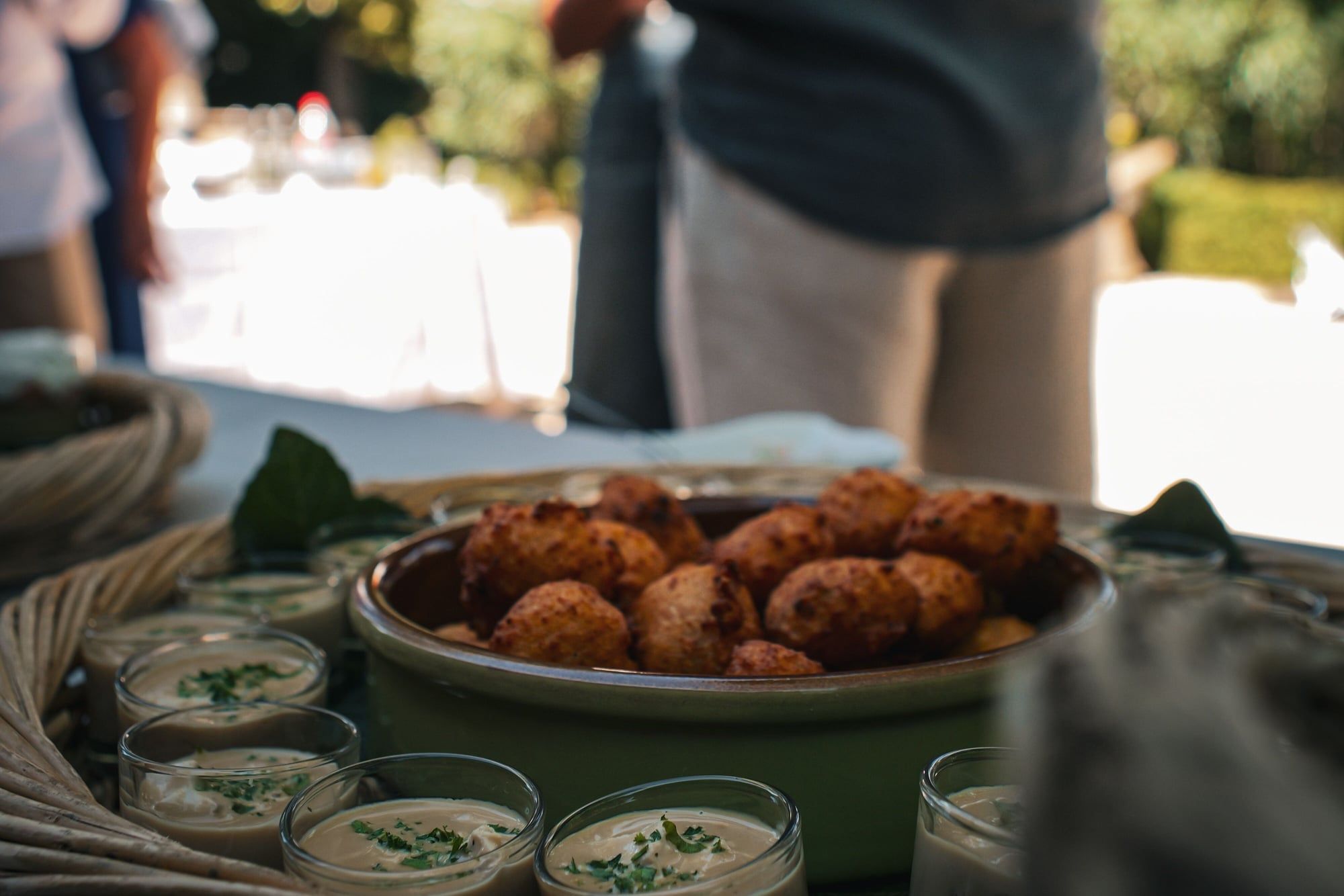 Beignets et verrines dressés sur une table en extérieur, un invité de dos